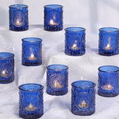 many blue glass candles are lined up on a white tablecloth with snow around them