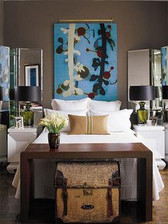 a bedroom with a large painting on the wall and a trunk in front of it