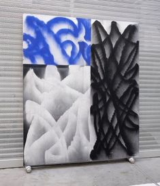 two black and white paintings are on display in front of a wall with blue spray paint