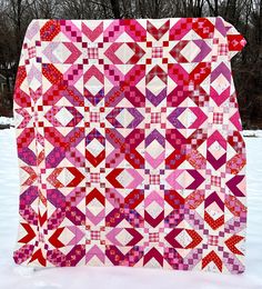 a pink and red quilt sitting on top of a snow covered ground with trees in the background