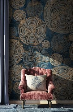 a pink chair sitting in front of a blue wall with gold circles on it's back