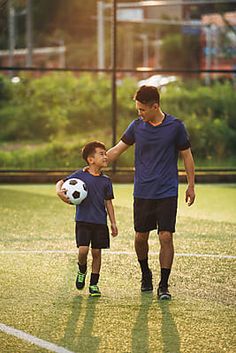 a man holding the hand of a young boy who is holding a soccer ball