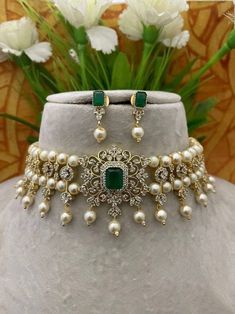 a necklace with pearls and emeralds on it next to some white flowers in front of a vase