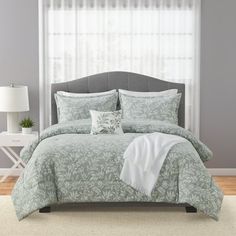 a bed in a bedroom next to a window with white curtains and a gray headboard