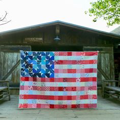 an american flag quilt hanging on the side of a wooden building in front of a picnic table