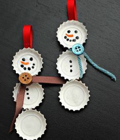 two snowmen made out of bottle caps on a black surface with red ribbon around them