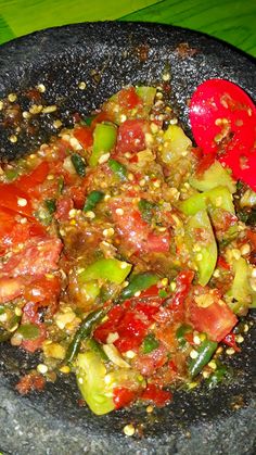 a black bowl filled with vegetables on top of a green table next to a red spoon