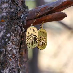 two gold earrings with mountains on them hanging from a tree