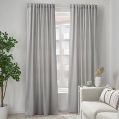 a living room with a white couch and gray curtains on the window sill, next to a potted plant