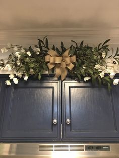 a bow is hanging on the back of a cabinet with flowers and greenery in it