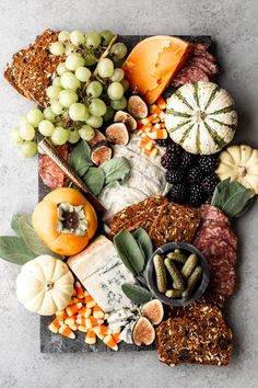 an assortment of cheeses, crackers, and fruits on a slate platter