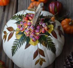 a white pumpkin decorated with flowers and leaves on a wooden table next to pine cones