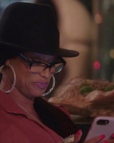 a woman wearing glasses and a hat looks at her cell phone while standing in front of a plate of food