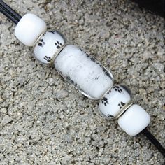 three white beads with black spots on them sitting on the ground next to a cord