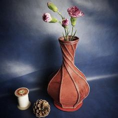 a vase with flowers in it next to a spool of thread and a pine cone