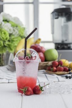 a drink with strawberries in it sitting on a table next to fruits and flowers