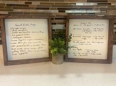 two framed pictures with writing on them in front of a tile wall and a potted plant