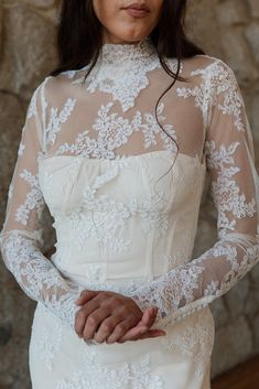 a woman in a white wedding dress standing next to a stone wall with her hands on her hips