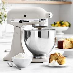 a white mixer sitting on top of a kitchen counter next to plates with cake and cupcakes