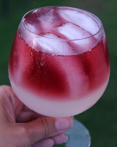 a hand holding a wine glass filled with red and white liquid on top of green grass