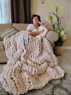 a woman sitting on top of a couch under a giant chunky knitted blanket