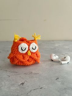 an orange crocheted owl hat and earphones on a gray surface with a white wall in the background