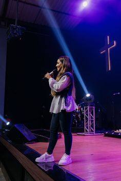 a woman standing on top of a stage with a microphone in her hand and lights behind her