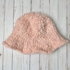 a pink sheepskin hat laying on top of a white wooden floor next to a wall