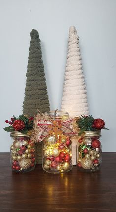 three jars filled with christmas decorations on top of a wooden table next to a small tree