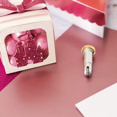 a white box with pink decorations and a silver pen on it next to a red gift bag