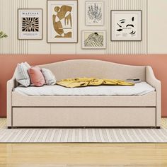 a white daybed sitting in front of a wall with pictures on it and pillows