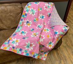 a pink quilt sitting on top of a brown couch