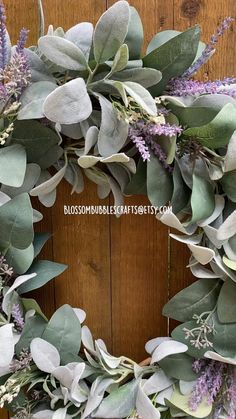 a close up of a wreath with purple flowers and green leaves on a wooden door