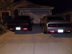 two cars parked next to each other in front of a house at night with the lights on