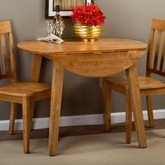 a small wooden table with two chairs and a vase filled with red flowers on it