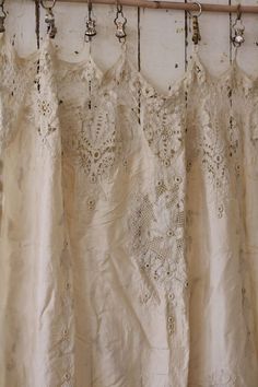 several white dresses hanging on a rack in front of a window with laces and beads