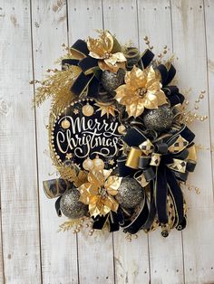 a black and gold wreath with merry christmas written on it sitting on a wooden surface