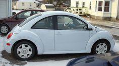 a small white car is parked in the snow next to another blue car and some houses