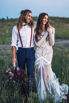 a man and woman are standing in the grass with flowers on their wedding day, wearing suspenders