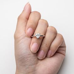 a woman's hand holding an engagement ring with a diamond in the middle, on a white background