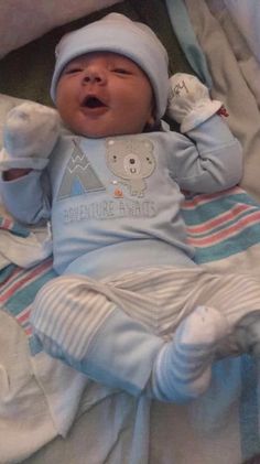 a baby laying on top of a bed wearing a blue outfit