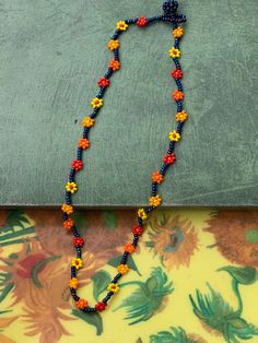 Dainty beaded necklace with daisy chain design with yellow, orange, & red flowers on blue vine. Falls perfectly below your collarbone and adds a touch of color to any outfit. Bead Flower Necklace, Bead Flower, Jaune Orange, Chain Design, Daisy Chain, Flower Necklace, Yellow Orange, Chain Styles, Orange Red