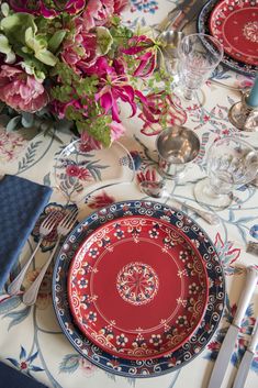 the table is set with red and blue plates, silverware, and pink flowers