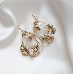 These handcrafted antique gold wedding earrings showcase a boho-inspired floral design, featuring delicate leaves and freshwater pearls. Expertly made to order, these hoop earrings add a touch of elegance and uniqueness to any bridal look. - Handcrafted in my PA studio - Genuine Austrian golden shadow crystal rock fabric leaves - Freshwater pearls - Antique gold leaves  - Available in rose gold, yellow gold or rhodium (silver) - Earrings measure 2.5 inches x 1-5/8 inch - Handcrafted in the US. - Floral Wedding Necklace, Vintage Wedding Earrings, Statement Wedding Earrings, Bridal Jewelry Gold, Jewelry For Bride, Wedding Earrings Vintage, Fabric Leaves, Statement Earrings Wedding, Antique Gold Earrings