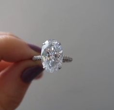 a close up of a person holding a ring with an oval cut diamond in it