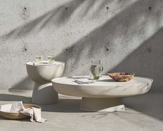 two white tables sitting next to each other near a wall and basket with food on it