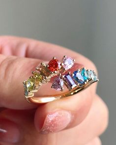 a woman's hand holding a gold ring with five different colored stones