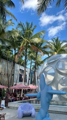 an inflatable elephant statue sitting on top of a cement ground next to palm trees