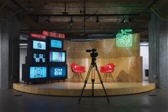 a camera is set up on a stage with chairs and televisions in the background