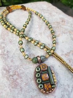 Lush earthy vibes abound in this petite 1" x .75" oval stainless steel copper colored bezel. Maize yellow glass square beads are featured, flanked by dark green beads and filati. African green opal and copper faceted beads add focal points in the 20" necklace with 2" extender and lobster clasp.
Necklace arrives in a violet burlap bag for easy gifting or protective storage.
Each is a one of a kind design of wearable art. I hope each brings joy to the recipient when worn. Green Copper Spiritual Necklace, Spiritual Green Copper Necklace, Artisan Jewelry With Czech Glass Oval Beads, Green Bohemian Oval Pendant Jewelry, Bohemian Nickel Free Oval Pendant Necklace, Green Artisan Oval Pendant Jewelry, Bohemian Nickel-free Oval Pendant Necklace, Artisan Green Oval Pendant Jewelry, Artisan Green Copper Necklace